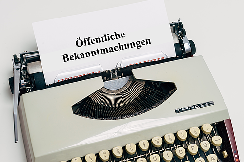 Schreibmaschine mit einem Blatt auf dem "Öffentliche Bekanntmachungen" steht