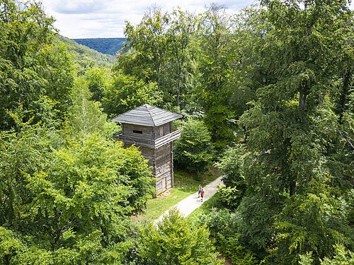Wanderer unterwegs auf dem Altmühltal-Panoramaweg sind gerade auf Höhe des Limesturms in Kipfenberg. Dieser steht inmitten grüner Bäume.