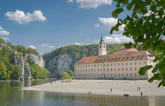 Das Kloster Weltenburg mit seinem Kieselstrand und der Donau, die  im Hintergrund durch den Donaudurchbruch hindurchfließt.