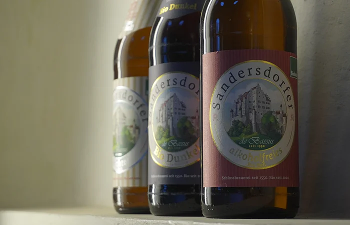Drei Bierflaschen der Marke Sandersdorfer auf einem Regal mit Etiketten mit Schlossabbildung.