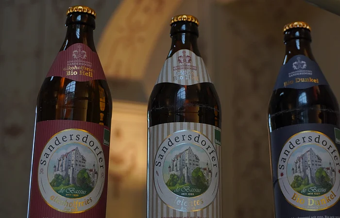 Drei Bierflaschen mit Etiketten der Marke Sandersdorfer, Sorten: alkoholfrei, leichtes, dunkel.