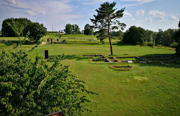 Grüne Wiesen mit Baum, Ruinenfundamenten und blauem Himmel mit Wolken im Hintergrund.